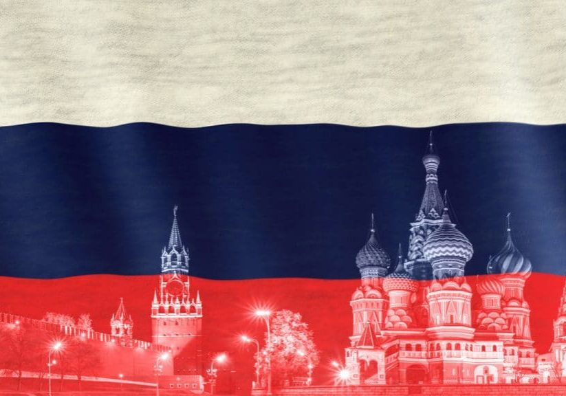 Closeup of Russian flag blown in the wind. Spasskaya town and St Basils cathedral Red Square silhouette at the bottom. Symbol of Russia.